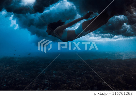 Woman swims under breaking wave with foam in blue ocean. Extreme duck dive under crashing waves Woman swims under breaking wave with foam in blue ocean. Extreme duck dive under crashing waves 115761268