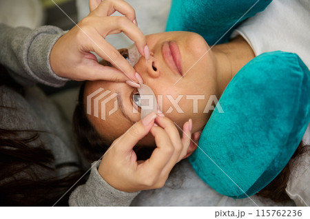 Beauty salon professional applying eyelash extensions to a client Beauty salon professional applying eyelash extensions to a client 115762236