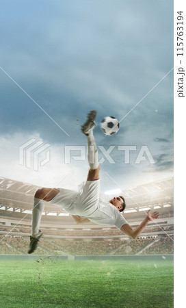 Vertical image of determined man, soccer player in white uniform hitting ball in jump and falling down, scoring goal. 3D render of stadium 115763194