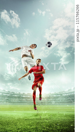 Dynamic, vertically-oriented photo. Soccer players in red and white jerseys in mid-air, competing for ball in stadium filled with cheering spectators. Dynamic, vertically-oriented photo. Soccer players in red and white jerseys in mid-air, competing for ball in stadium filled with cheering spectators. 115766266