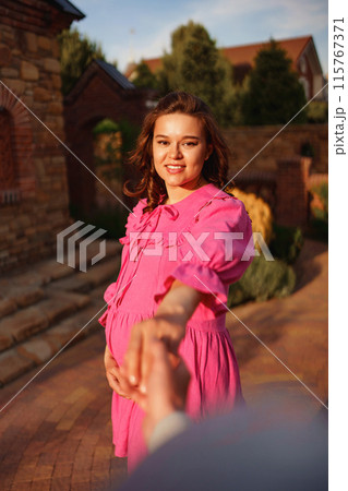 pregnant brunette woman in pink dress holding man's hand and following him. pregnant brunette woman in pink dress holding man's hand and following him. 115767371