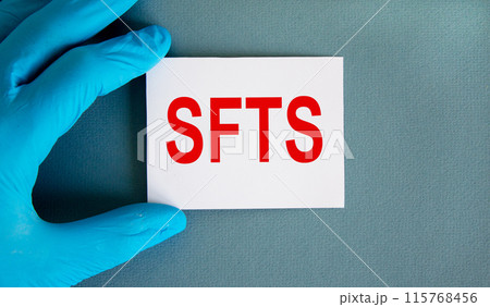 Hand in blue glove with white card. Concept word 'SFTS'. COVID-19 Pandemic Coronavirus concept. Beautiful blue background. Hand in blue glove with white card. Concept word 'SFTS'. COVID-19 Pandemic Coronavirus concept. Beautiful blue background. 115768456