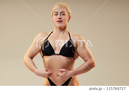 Medium shot of sportswoman with solid muscles performing front lat spread pose highlighting back and shoulder width, overall torso silhouette isolated in studio on neutral background, copy space 115768727