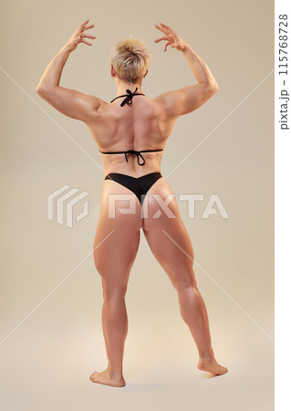 Vertical shot of athletic female model in back double biceps pose showing back size and symmetry in tandem with arms, shoulders, hamstrings and calf isolated in studio on neutral background 115768728
