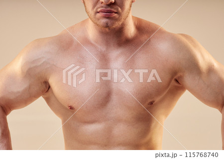 Cropped shot of male bodybuilder giving front lat spread pose. Bare muscular chest of sportsman isolated on neutral background, copy space 115768740
