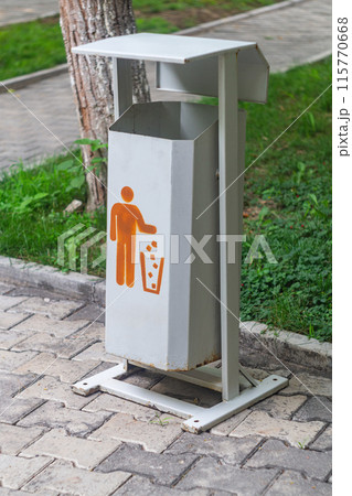 Vertical shot of a metal trash can, painted in a monotonous gray color with the iconic symbol of the silhouette of a man throwing garbage into a trash can. Inventory of the city park. 115770668