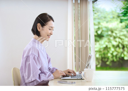 リビングでコーヒーを飲みながらパソコンを見るミドル女性 115777575