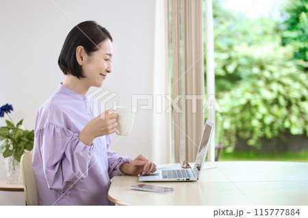 リビングでコーヒーを飲みながらパソコンを見るミドル女性 リビングでコーヒーを飲みながらパソコンを見るミドル女性 115777884