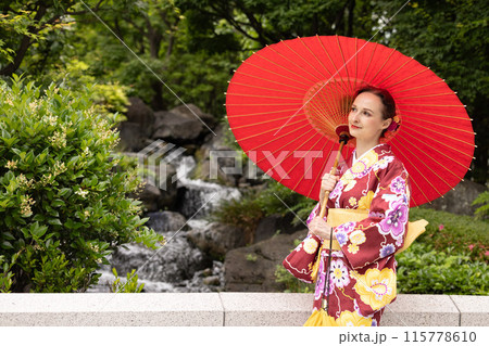 日本庭園で赤い和傘を差す着物姿の外国人女性観光客 115778610