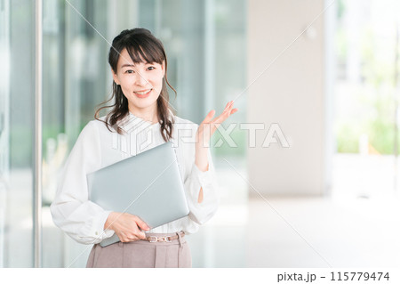 ビルの前でノートパソコンを持つビジネスウーマン・ワーキングママ（案内・こちら・紹介） 115779474