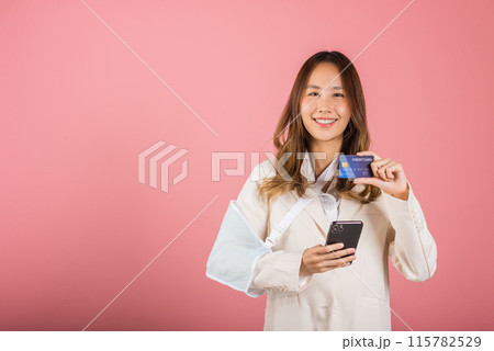 Woman confident smile broken arm after accident and wear arm splint for treatment she emergency pay medical bills by credit card and mobile phone, Asian female sling support hand isolated background 115782529