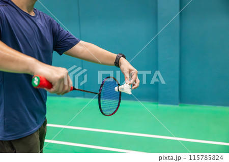 Badminton player hand serving holding shuttlecock and professional badminton racket at indoor sport badminton court Badminton player hand serving holding shuttlecock and professional badminton racket at indoor sport badminton court 115785824