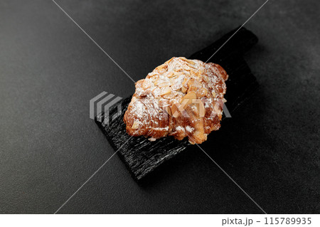 Almond croissant. puff pastry, delicate frangipane cream with almonds, enriched with butter. On top, the croissant has a hint of almond flakes and powdered sugar. on a black cutting board Almond croissant. puff pastry, delicate frangipane cream with almonds, enriched with butter. On top, the croissant has a hint of almond flakes and powdered sugar. on a black cutting board 115789935