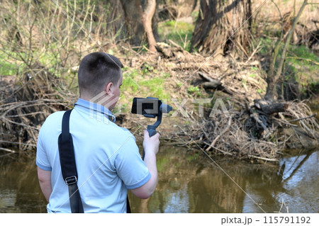 A young man videotaping on a smartphone. Uses gimbal to get smooth footage. Closely watching the movie shooting. 115791192