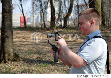A young man videotaping on a smartphone. Uses gimbal to get smooth shots. Controls the recording by touching the screen. A young man videotaping on a smartphone. Uses gimbal to get smooth shots. Controls the recording by touching the screen. 115791478