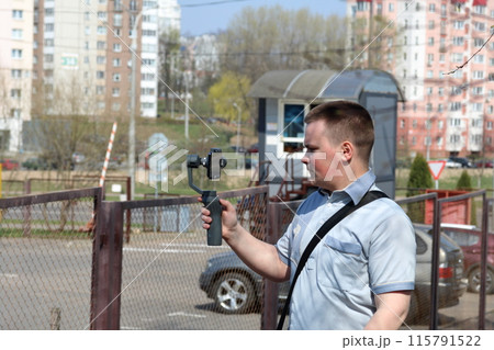 A young man videotaping on a smartphone. Uses gimbal to get smooth footage. Closely watching the movie shooting. 115791522