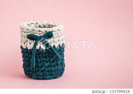 Cozy Teal and White Knitted Basket with Dark Teal Ribbon on Pink Background Cozy Teal and White Knitted Basket with Dark Teal Ribbon on Pink Background 115794018