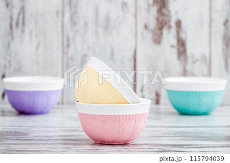Colorful bowls with knitted patterns, stacked and arranged on a wooden surface with a rustic background. 115794039