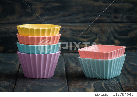 Colorful silicone baking cups on a dark blue wooden surface, in various pastel colors including pink, yellow, mint green, and purple. 115794040