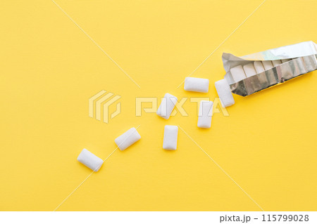 White chewing gum pads spilled out of a foil package on a yellow background 115799028