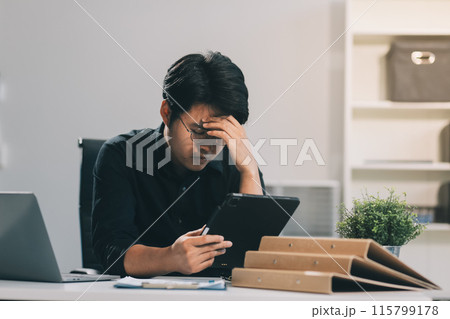Frustrated Asian young businessman worker working on table in office. Busy employee worker people feel tired and headache from late work and overwork job document on computer desk at company workplace 115799178