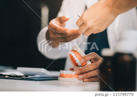 A dentist is using specialized dental equipment to inspect dentures to study the anatomy of the teeth before using the knowledge to treat patients, Dentures are being studied by oral specialists. 115799770