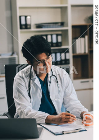 A dentist is using specialized dental equipment to inspect dentures to study the anatomy of the teeth before using the knowledge to treat patients, Dentures are being studied by oral specialists. 115799960