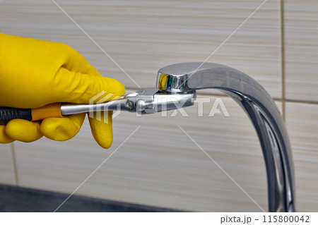 A plumber wearing yellow rubber gloves changes the faucet aerator. Regular repairs and replacement of water pipes 115800042