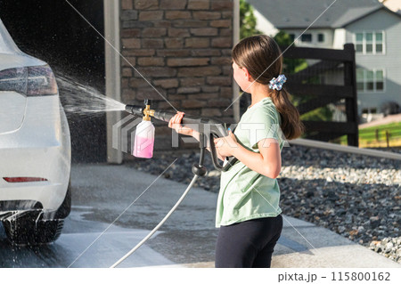 A young girl enthusiastically assists in washing the family's electric car in their suburban driveway. 115800162