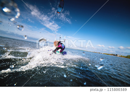 Attractive young Caucasian female kiteboarder doing a trick at sunset with splashes and a smile. Wide angle. Deep dive 115800389