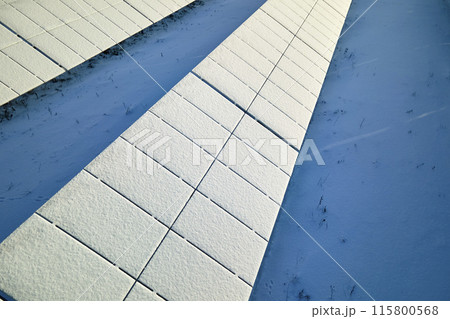 Aerial view of snow covered sustainable electric power plant with rows of solar photovoltaic panels for producing clean electrical energy. Low effectivity of renewable electricity in northern winter Aerial view of snow covered sustainable electric power plant with rows of solar photovoltaic panels for producing clean electrical energy. Low effectivity of renewable electricity in northern winter 115800568