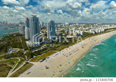 Travel destination in United States. South Beach sandy surface with tourists relaxing on hot Florida sun. Tourism infrastructure in southern USA. Miami Beach city with high luxury hotels and condos Travel destination in United States. South Beach sandy surface with tourists relaxing on hot Florida sun. Tourism infrastructure in southern USA. Miami Beach city with high luxury hotels and condos 115800706