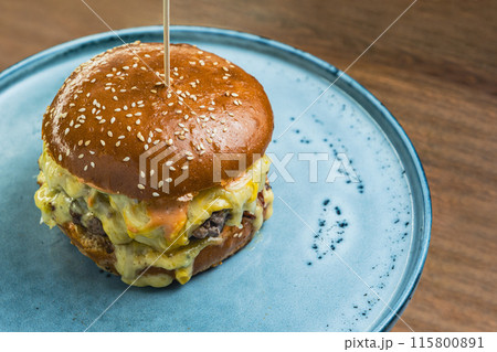 Craft cheeseburger with melted cheese served on a plate on a wooden table Craft cheeseburger with melted cheese served on a plate on a wooden table 115800891