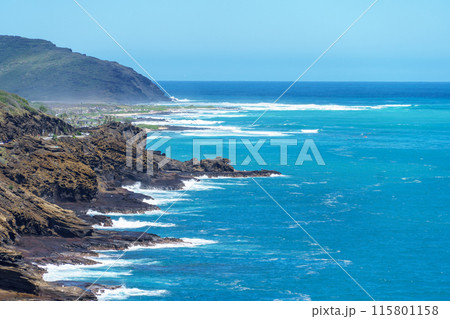 A scenic view of a cliff facing the ocean with waves breaking on the sandy beach 115801158