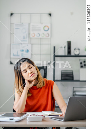 Woman in red top at desk with laptop, experiencing neck pain and fatigue in modern office setting. 115806301