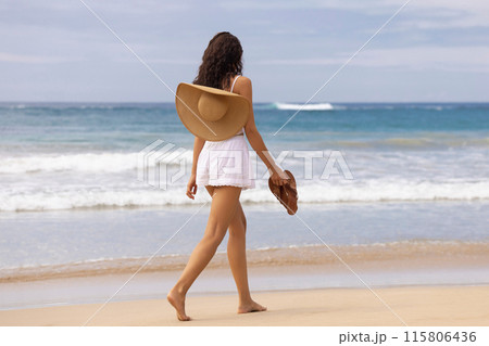 Woman with Sun Hat and Sandals Walking Along Sandy Beach Woman with Sun Hat and Sandals Walking Along Sandy Beach 115806436