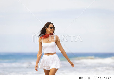 Woman in White Outfit Strolling on Beach 115806457