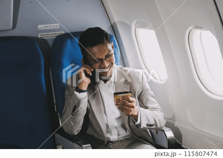 Businessman holding credit card and looking at camera near laptop in private jet Businessman holding credit card and looking at camera near laptop in private jet 115807474