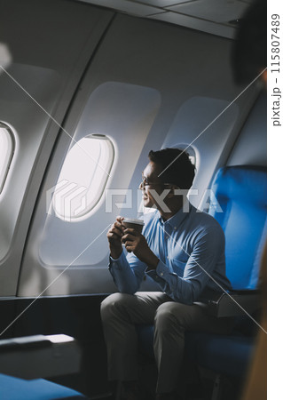 Asian businessman enjoying enjoys a coffee comfortable flight while sitting in the airplane cabin, Passengers near the window. Asian businessman enjoying enjoys a coffee comfortable flight while sitting in the airplane cabin, Passengers near the window. 115807489