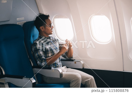 Asian man enjoying enjoys a coffee comfortable flight while sitting in the airplane cabin, Passengers near the window. Asian man enjoying enjoys a coffee comfortable flight while sitting in the airplane cabin, Passengers near the window. 115808876
