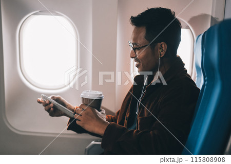 Happy curly man use phone and listens to music headphones on board airplane during flight. 115808908