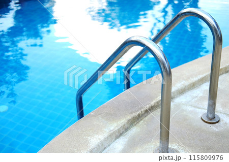 Stainless steel handrail in blue water and ceramic tiles in swimming pool outdoor in garden of resort and hotel 115809976