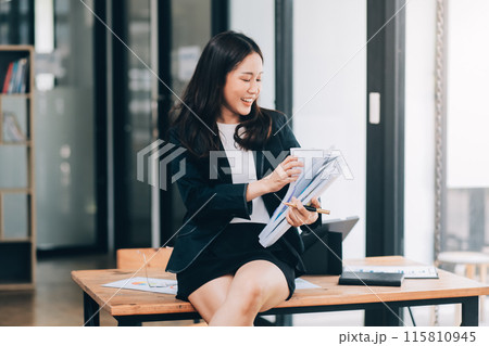 Asian businesswoman talking on phone, using laptop, looking at screen, entrepreneur manager consulting client by call, looking at computer screen, discussing project, reading information 115810945