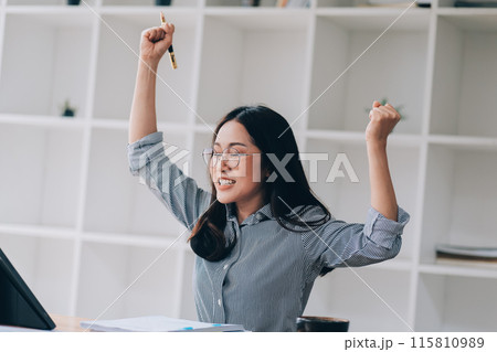 Happy asian woman office worker feeling excitement raising fists celebrates career ladder promotion or reward, businesswoman sitting at desk receive online news, great results successful work concept. 115810989