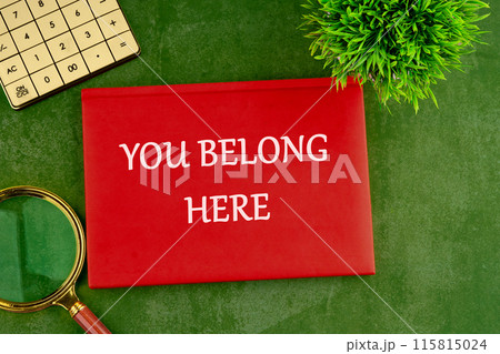 YOU BELONG HERE TEXT on a red business notebook on a gorgeous green background YOU BELONG HERE TEXT on a red business notebook on a gorgeous green background 115815024