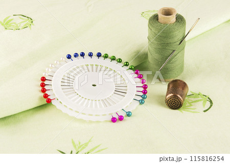 Dressmaker pins with a spool of thread and a thimble on the material 115816254