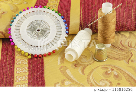 Two spools of thread with a needle and thimble copper lie on curtain fabrics 115816256