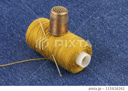 The coil of yellow threads with a metal needle and metal thimble on blue denim 115816262