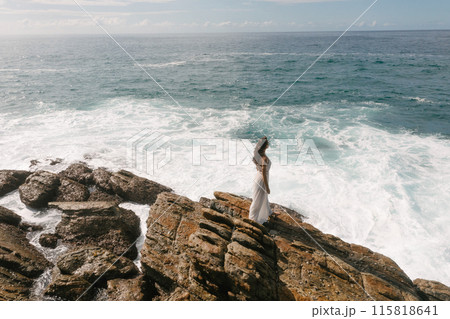 Woman in White Dress Standing on Rocky Coastline 115818641