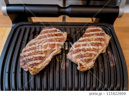 Chef at the kitchen preparing beef steaks on the home electric grill 115822609